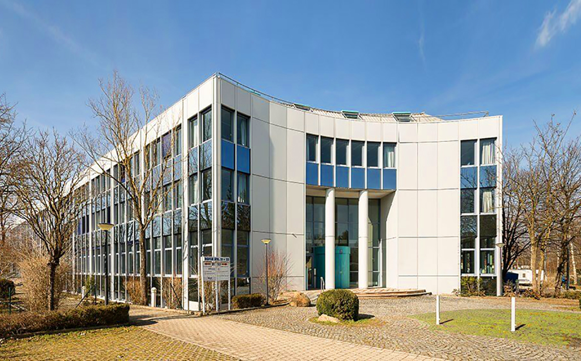 Zu sehen ist der Eingangsbereich des Quartiers HOFER STRASSE mit Blick vom Hof auf die Front eines Gebäudes mit Bäumen und einem Fußweg.