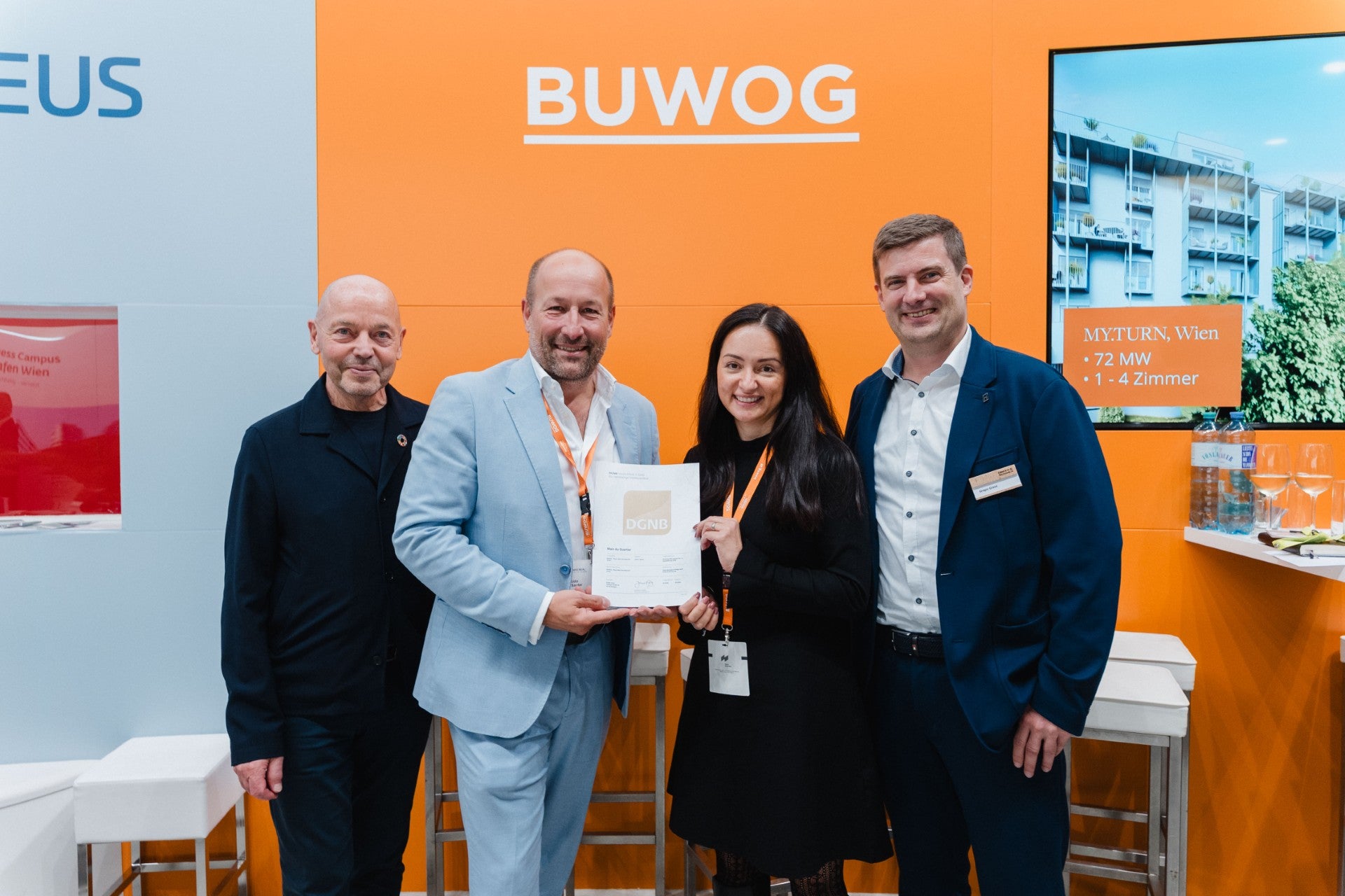 Vier Personen präsentieren gemeinsam eine DGNB-Urkunde am BUWOG-Messestand.