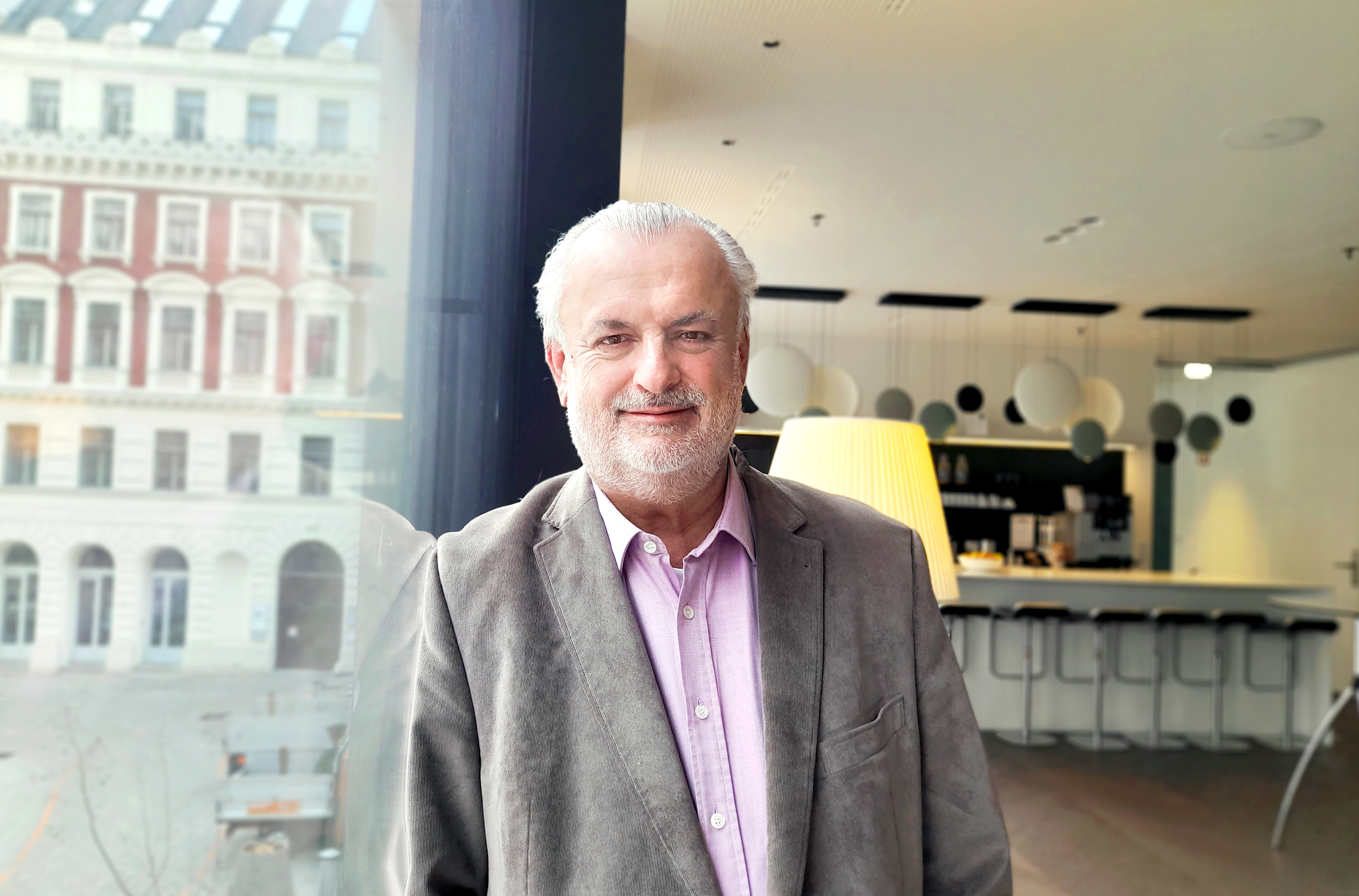 You can see an older man with short white hair, a grey blazer and a rose-coloured shirt