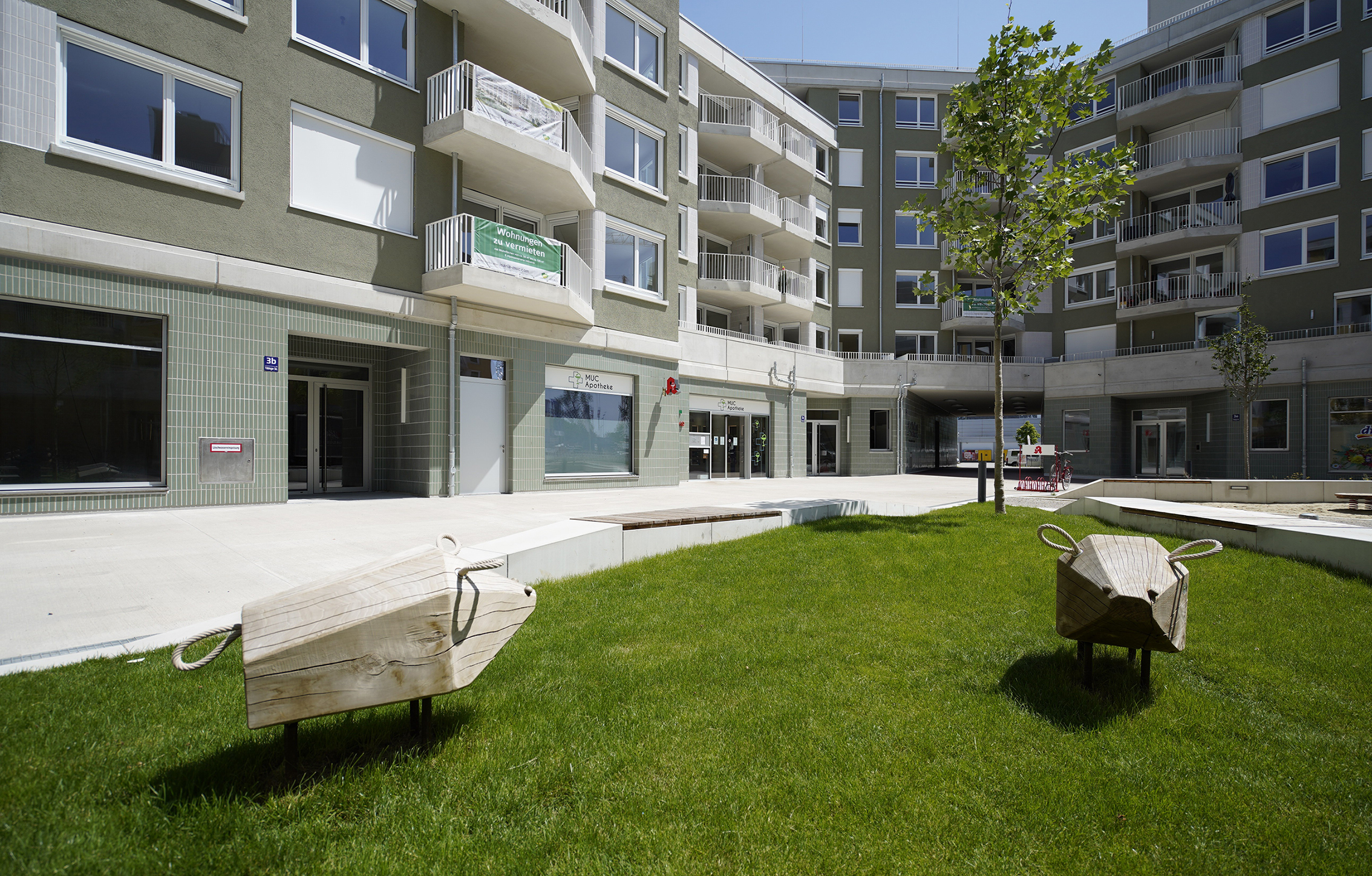 Zu sehen ist das Projekt GREENLEVELS mit Blick vom Hof aus auf einen kleinen Spielplatz, sowie auf Geschäfte im Erdgeschoss.