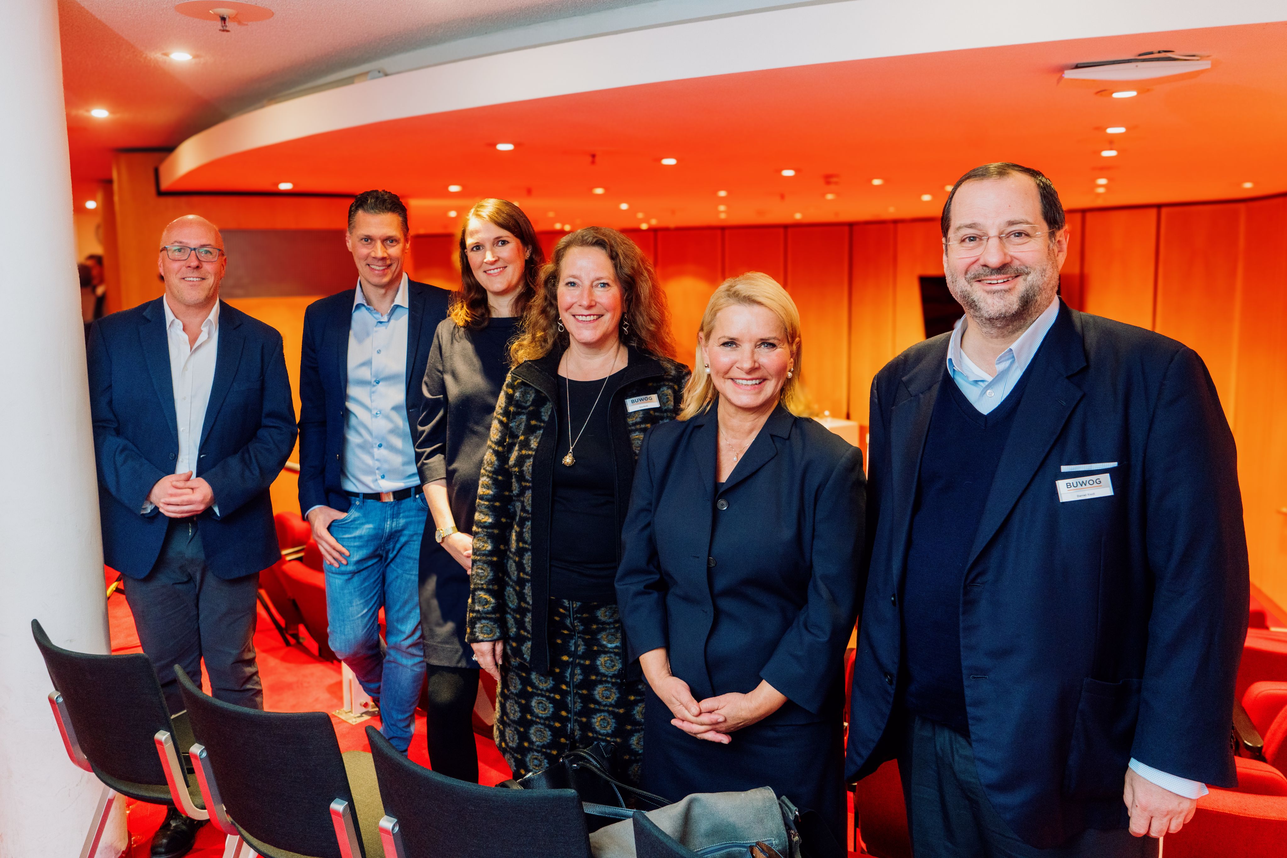 You can see 6 people, 3 men and 3 women with a red-orange background.