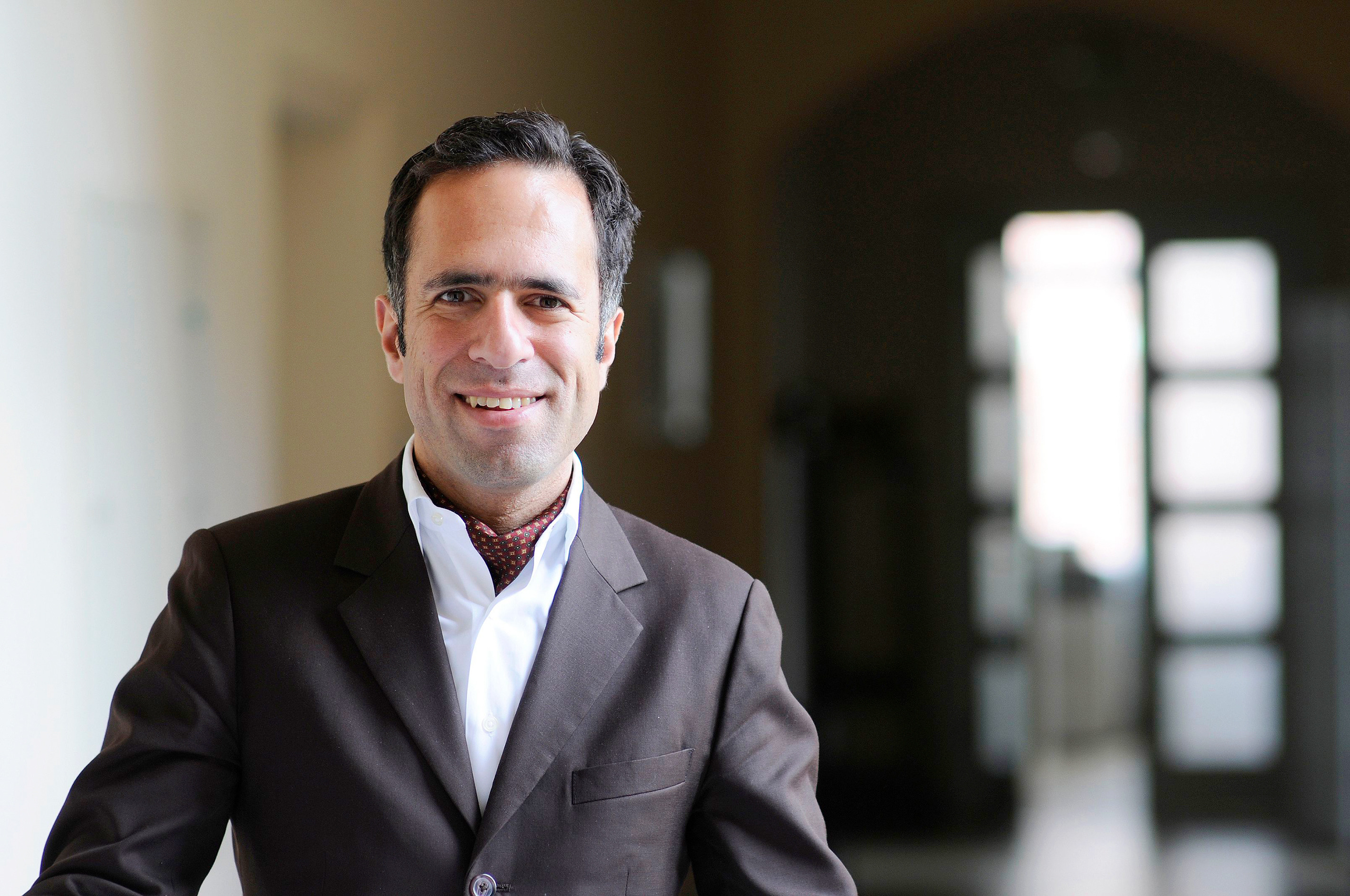 You can see a man with short black hair, a black blazer and a white shirt